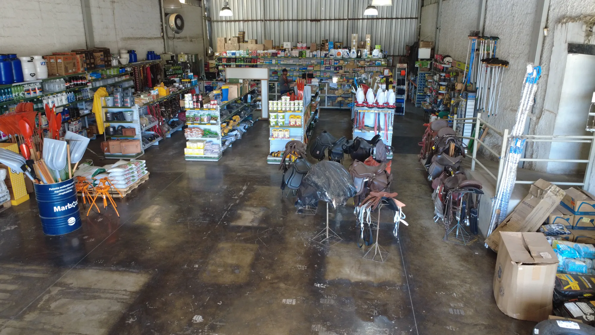 Interior do armazém da COOP GBH, com prateleiras de produtos, selas e ferramentas